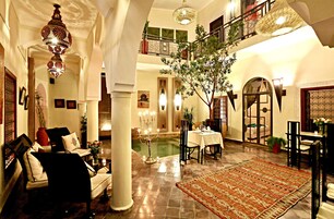 A spacious lobby with a high ceiling, a chandelier, a dining area, and a staircase leading to an upper level.