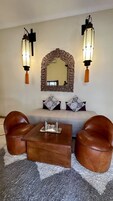 A room with a sofa, two leather armchairs, a coffee table, a decorative mirror, and wall-mounted lights.