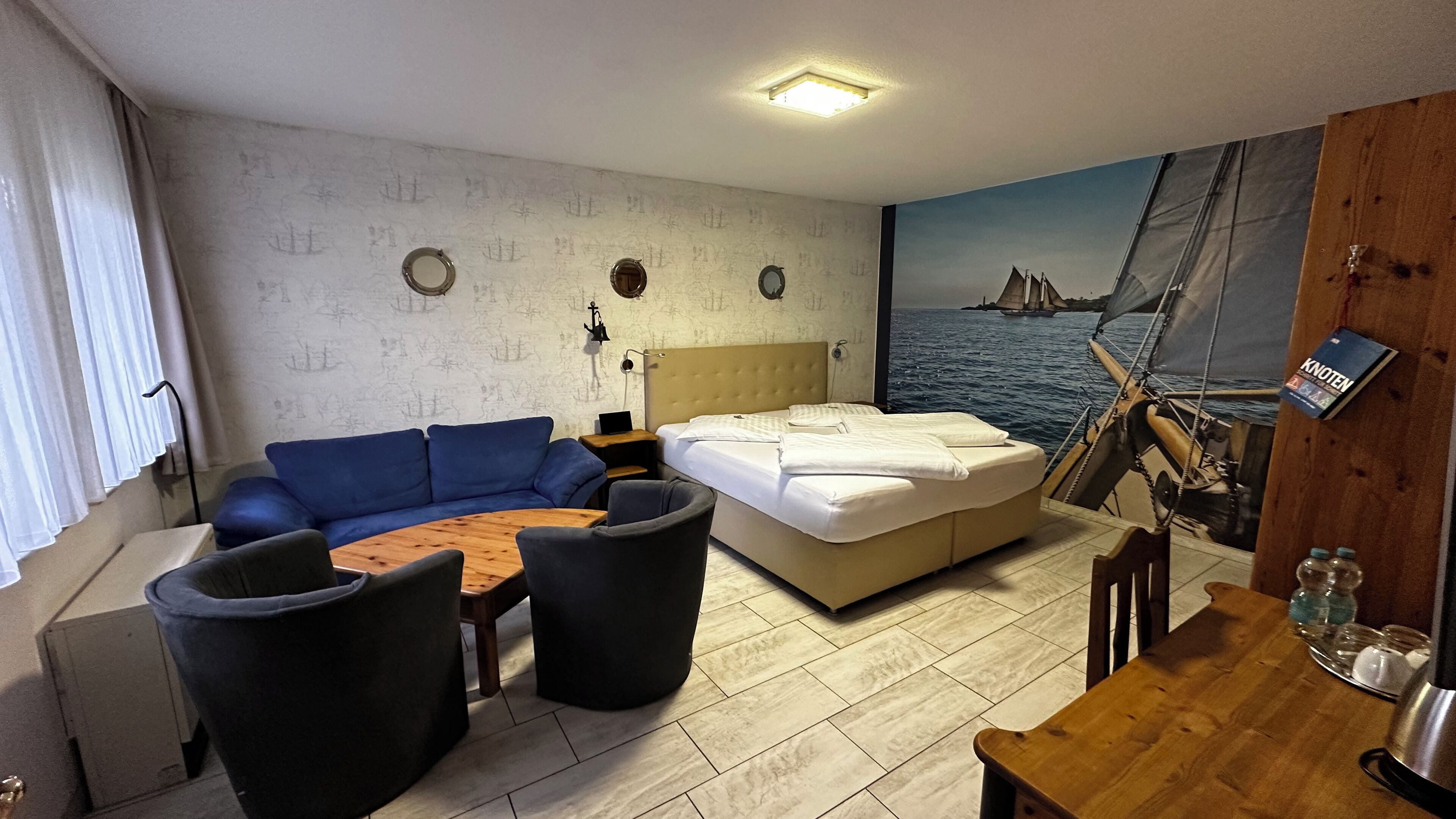 Una habitación acogedora con una cama, un sofá azul, una mesa de centro redonda y una mesa de madera con sillas.