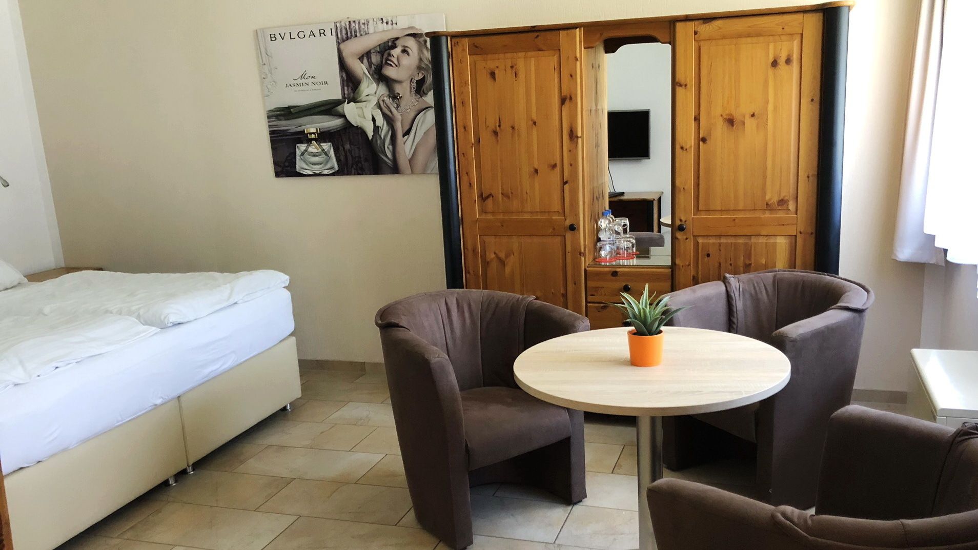Une chambre à coucher comprenant un lit, deux fauteuils, une petite table ronde avec une plante et une armoire en bois.