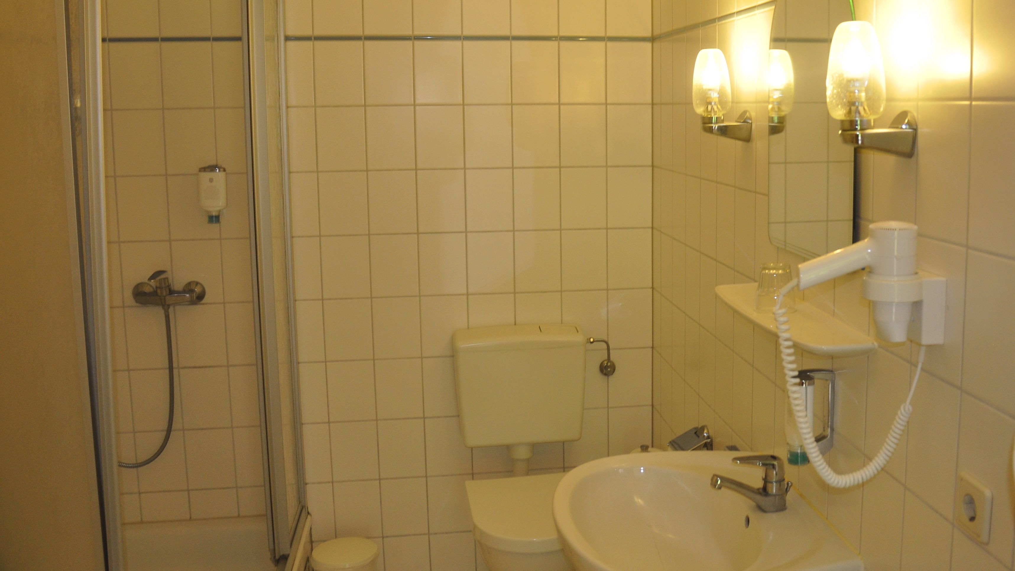 Baño con ducha, inodoro, lavabo y espejo con luces.