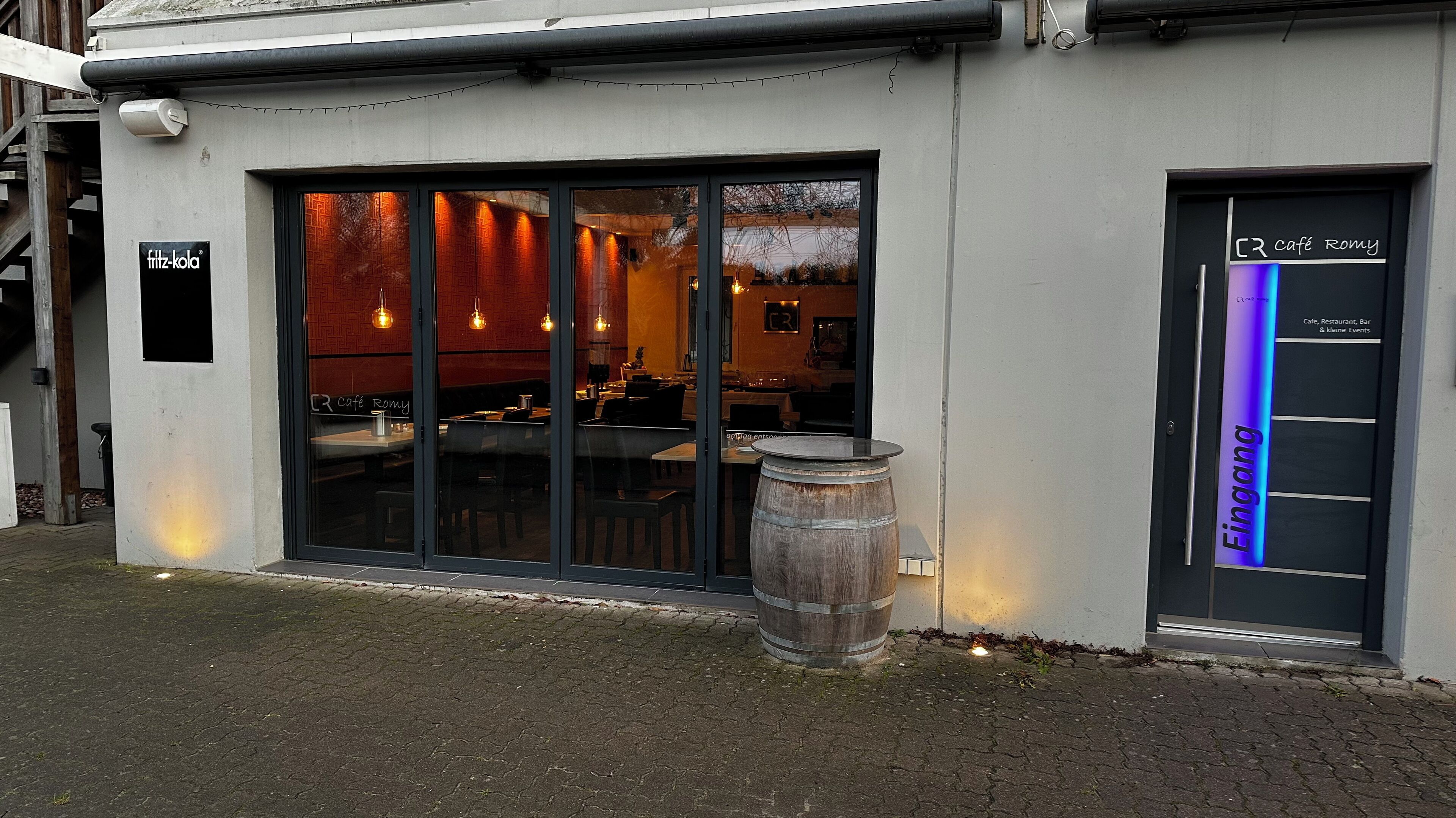 Un edificio con un letrero que dice "cafe romy" y un barril de madera grande en el exterior.