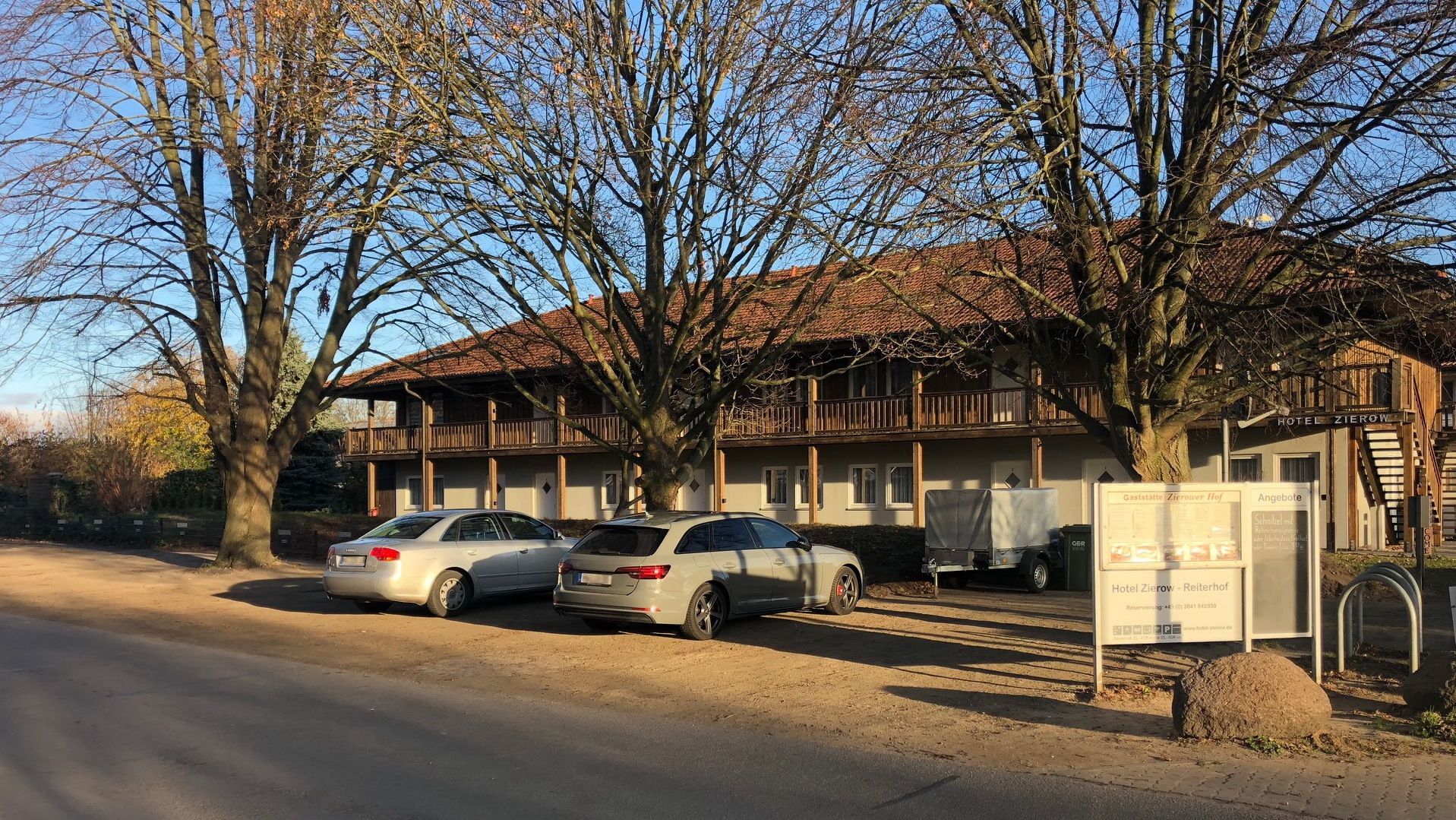 Ein Hotel mit traditioneller Holzfassade, zwei geparkte Autos und einer Schautafel mit Informationen.