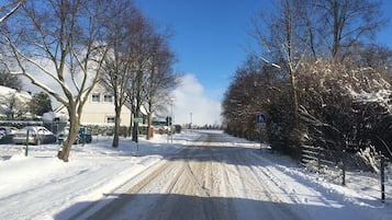 A snow-covered road with parked cars and leafless trees.