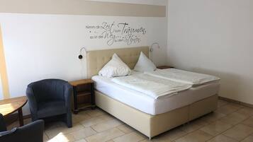 A neatly arranged hotel room with a bed, two bedside tables, a chair, and a wall with a motivational quote.