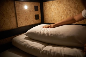 A bunk bed with a hand on the top pillow, wooden walls, and a small window with a light source. - Haystack Hostel (Edinburgh)