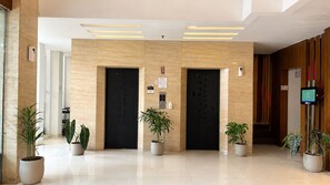 A modern lobby with two elevators, potted plants, a digital display, and a 'No Smoking' sign. - Vio Cihampelas (Bandung)