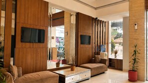 A modern living room with a sofa, a coffee table, a TV mounted on the wall, and a large mirror. - Vio Cihampelas (Bandung)