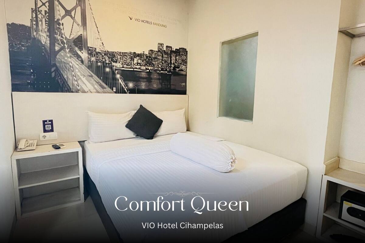 A hotel room with a bed, a nightstand, a phone, and a poster of a bridge.