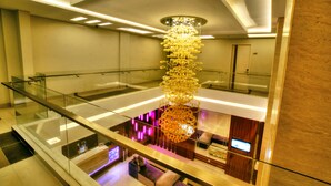Un hall d’hôtel moderne avec un lustre central, des rampes en verre et un espace salon équipé d’un téléviseur.