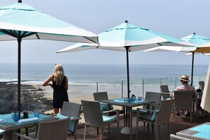 An outdoor seating area with tables and chairs, overlooking a beach. - Watersmeet Hotel (Woolacombe)