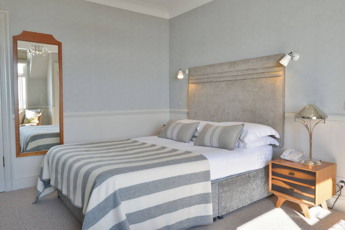 Ein aufgeräumtes Schlafzimmer mit einem großen Bett, Nachttischlampen, einem Nachttisch und einem Spiegel.