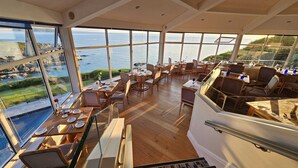 Un comedor amplio con ventanas grandes que ofrecen vistas al océano, suelo de madera y una variedad de opciones de asientos.