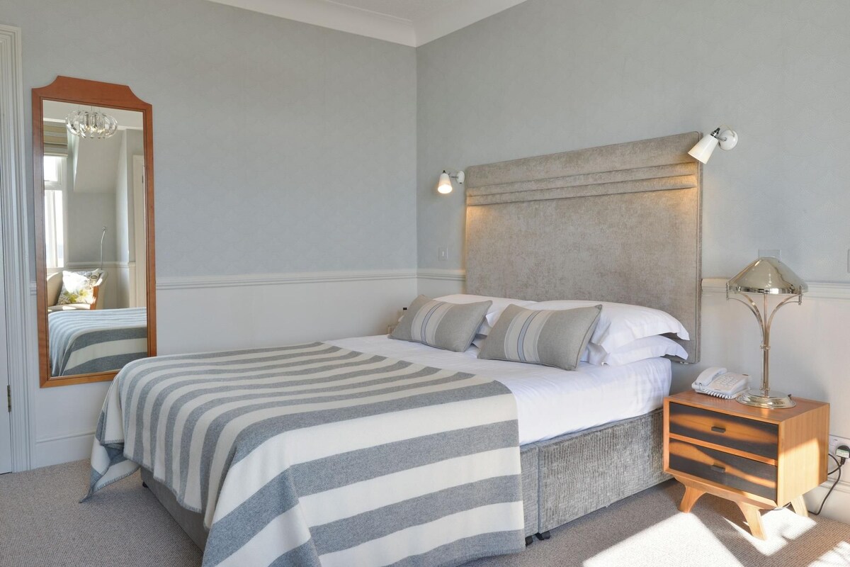 Un dormitorio con cama, una mesita de noche con lámpara, un espejo y cabecero.