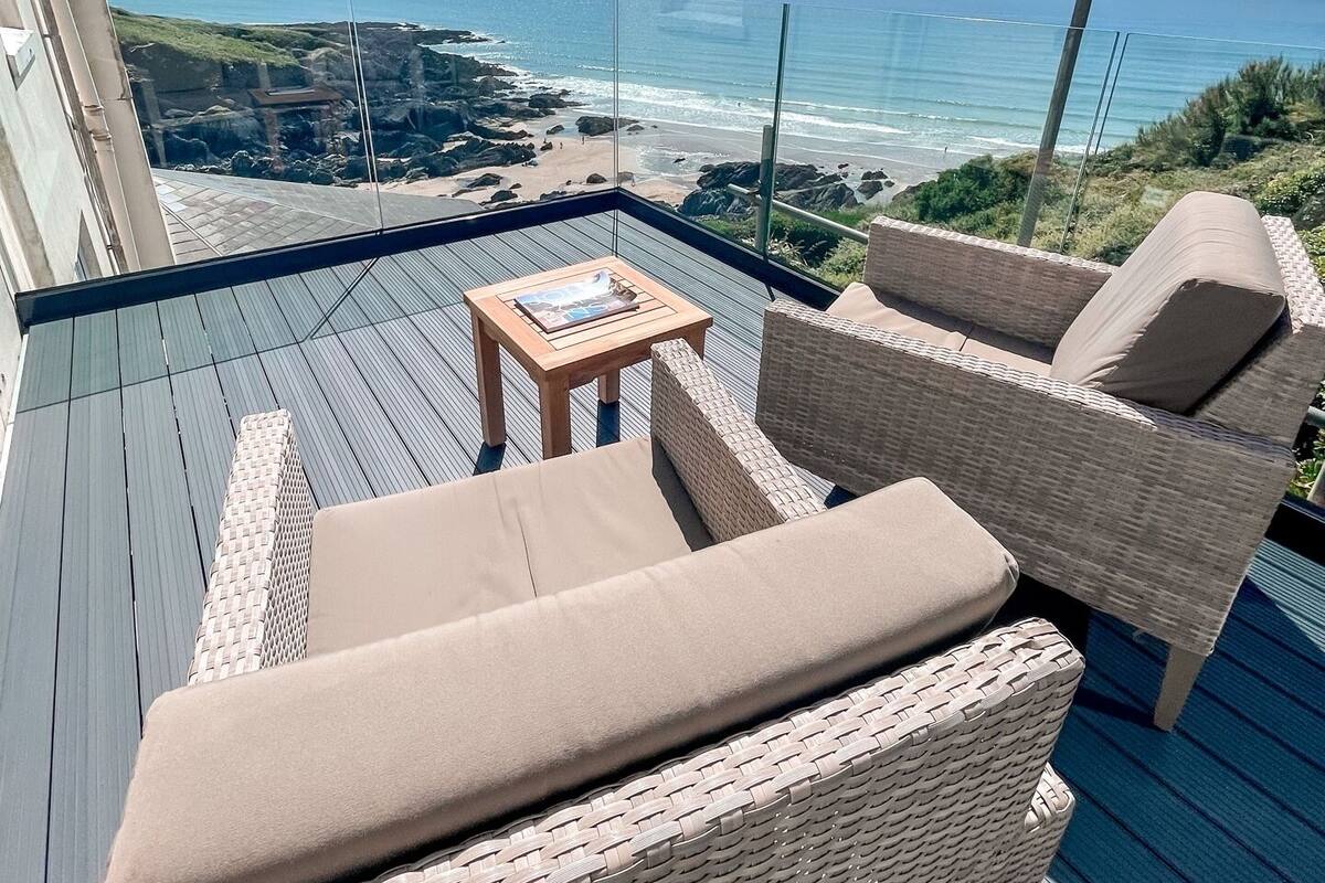 Ein Balkon mit Korbmöbeln, einem kleinen Tisch und Blick auf das Meer und die Küste.