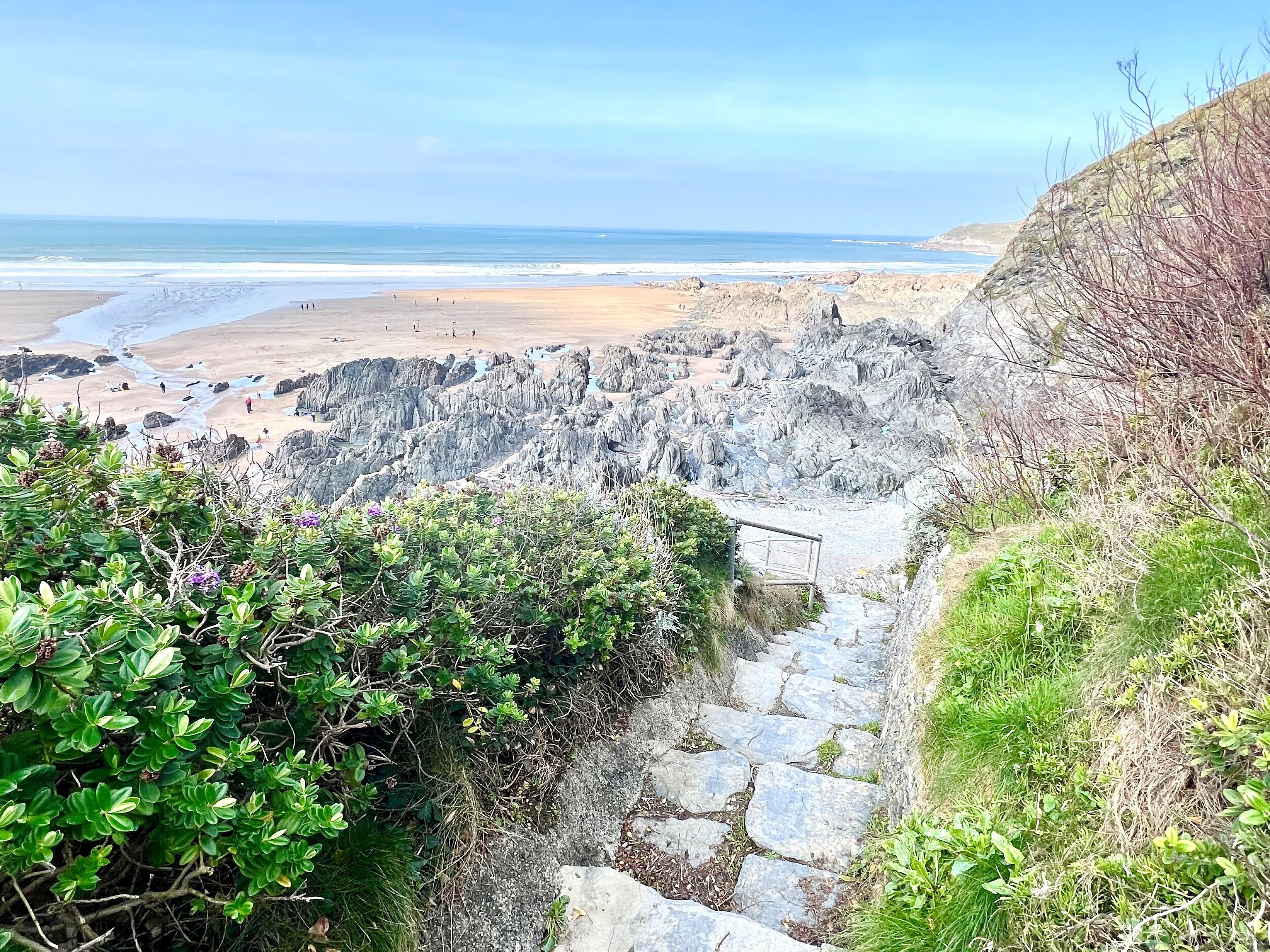 A coastal path leading to a rocky beach with a clear view of the ocean.