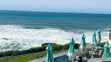 A poolside area with a view of the ocean, outdoor seating, and umbrellas.