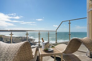 A balcony with wicker furniture, a table with a bottle and glasses, and a view of the ocean. - Watersmeet Hotel (Woolacombe)