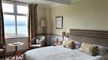 Habitación de hotel con una cama grande, una silla, una mesita, una lámpara y vistas al mar.
