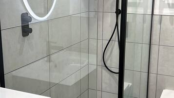 Et moderne badeværelse med en bruseniche i glas, en hvid vask og et toilet.