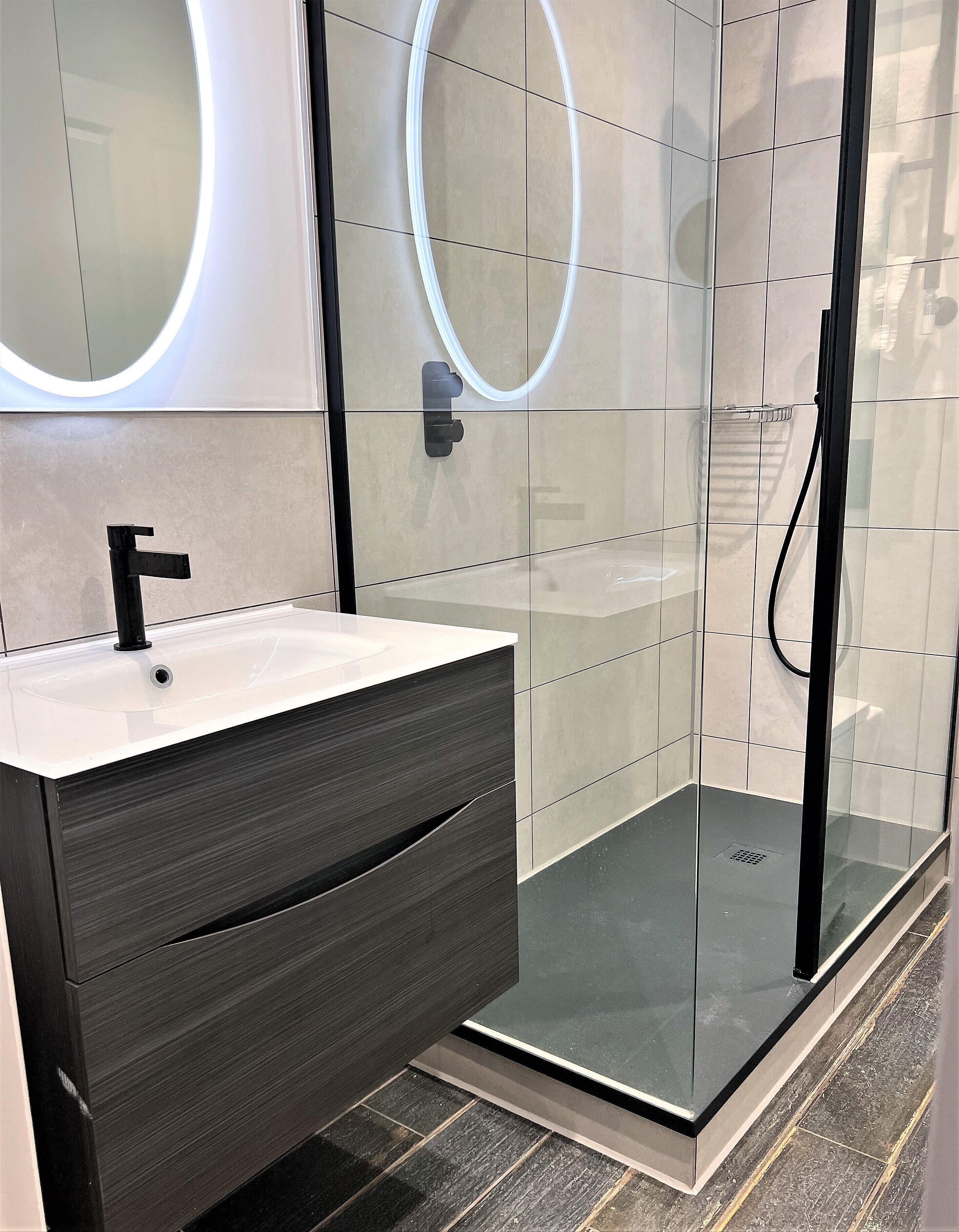 Ein modernes Badezimmer mit Duschkabine aus Glas, Waschbecken in Weiß mit schwarzem Wasserhahn und einem dunklen Holzschrank.