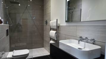 Un baño moderno con ducha de vidrio, lavamanos blanco y un inodoro.
