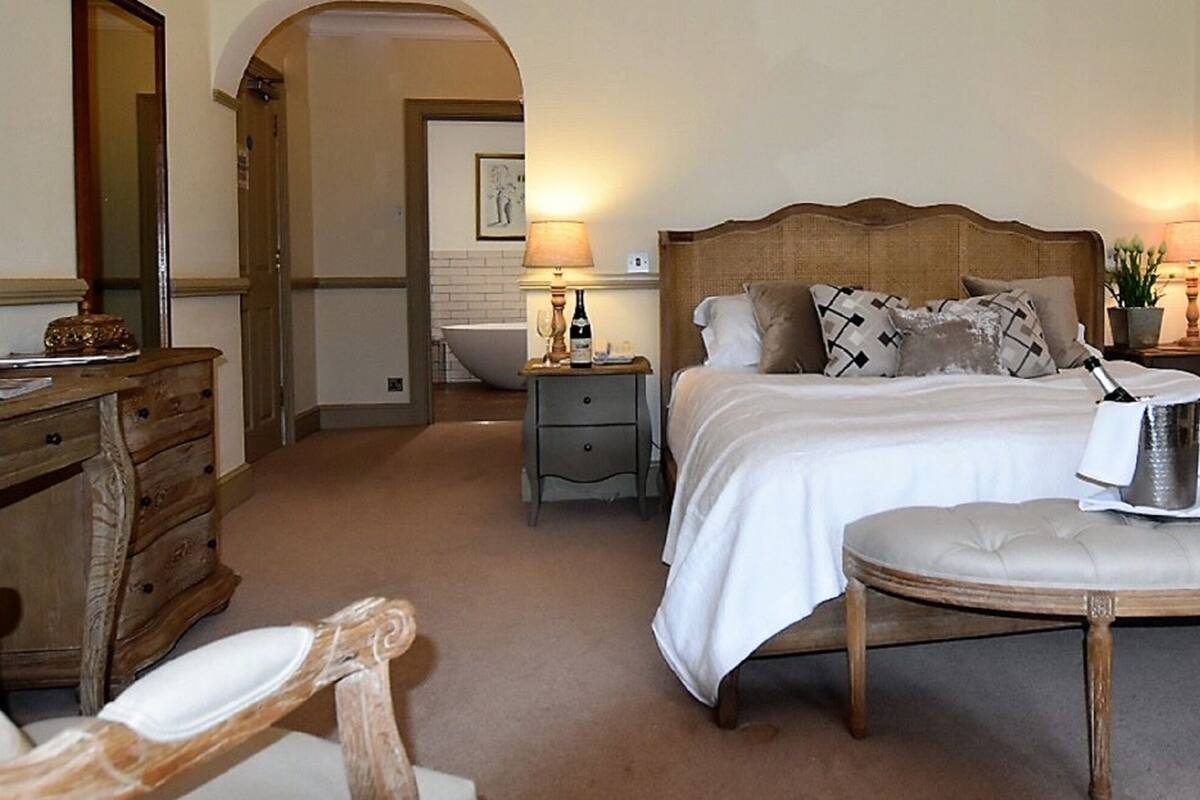 Ein Hotelzimmer mit Bett, Nachttischen, Schreibtisch, Stuhl und einem kleinen Tisch mit Flasche und Glas.