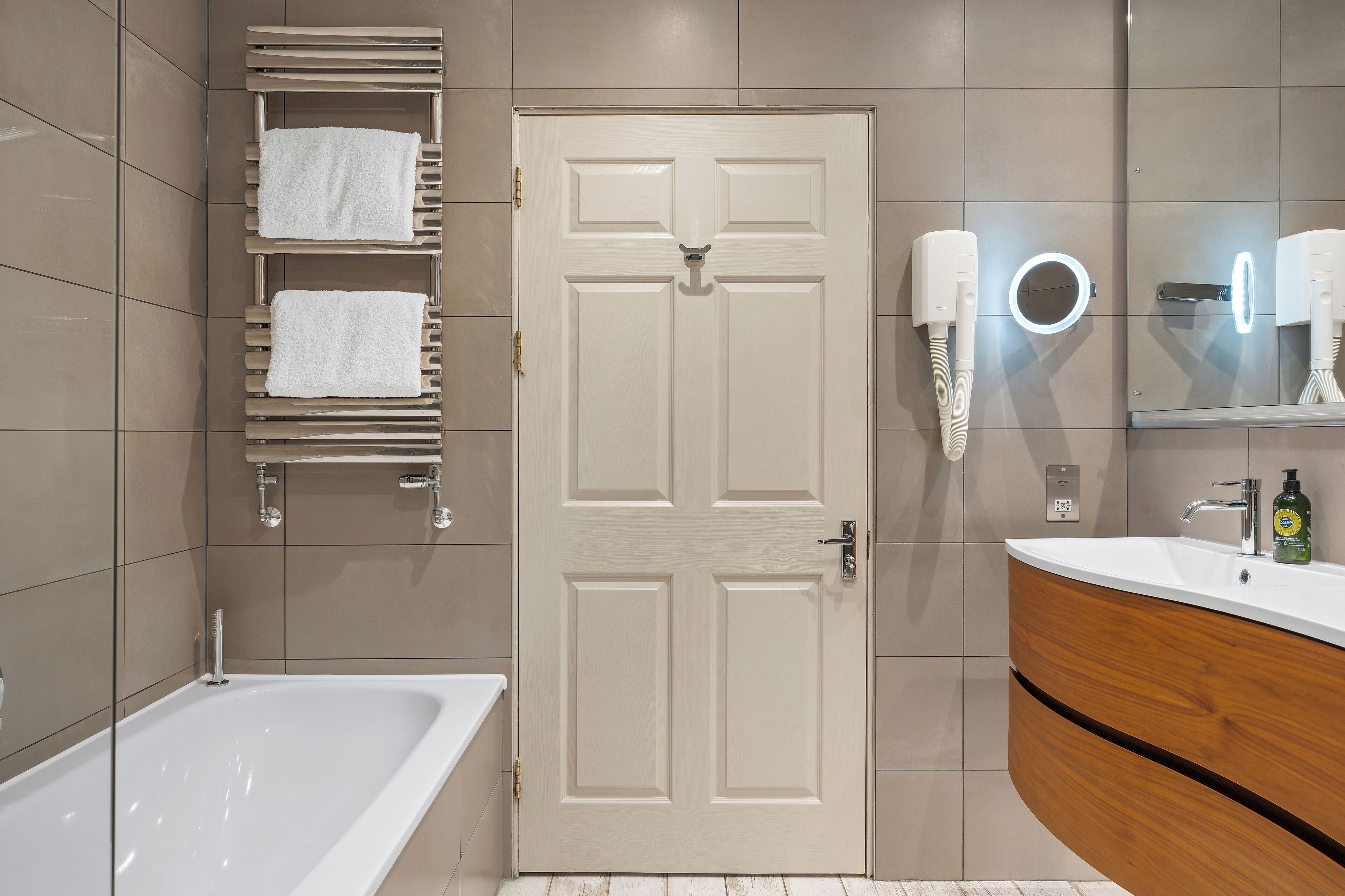 Un baño moderno con una bañera blanca, un tocador de madera con un espejo y un perchero con dos toallas blancas.