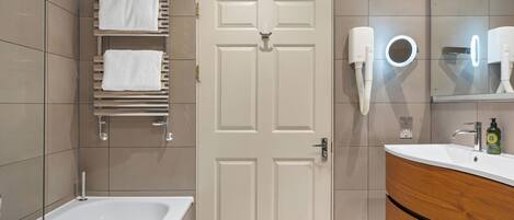 Un baño moderno con una bañera blanca, un tocador de madera con un espejo y un perchero con dos toallas blancas.