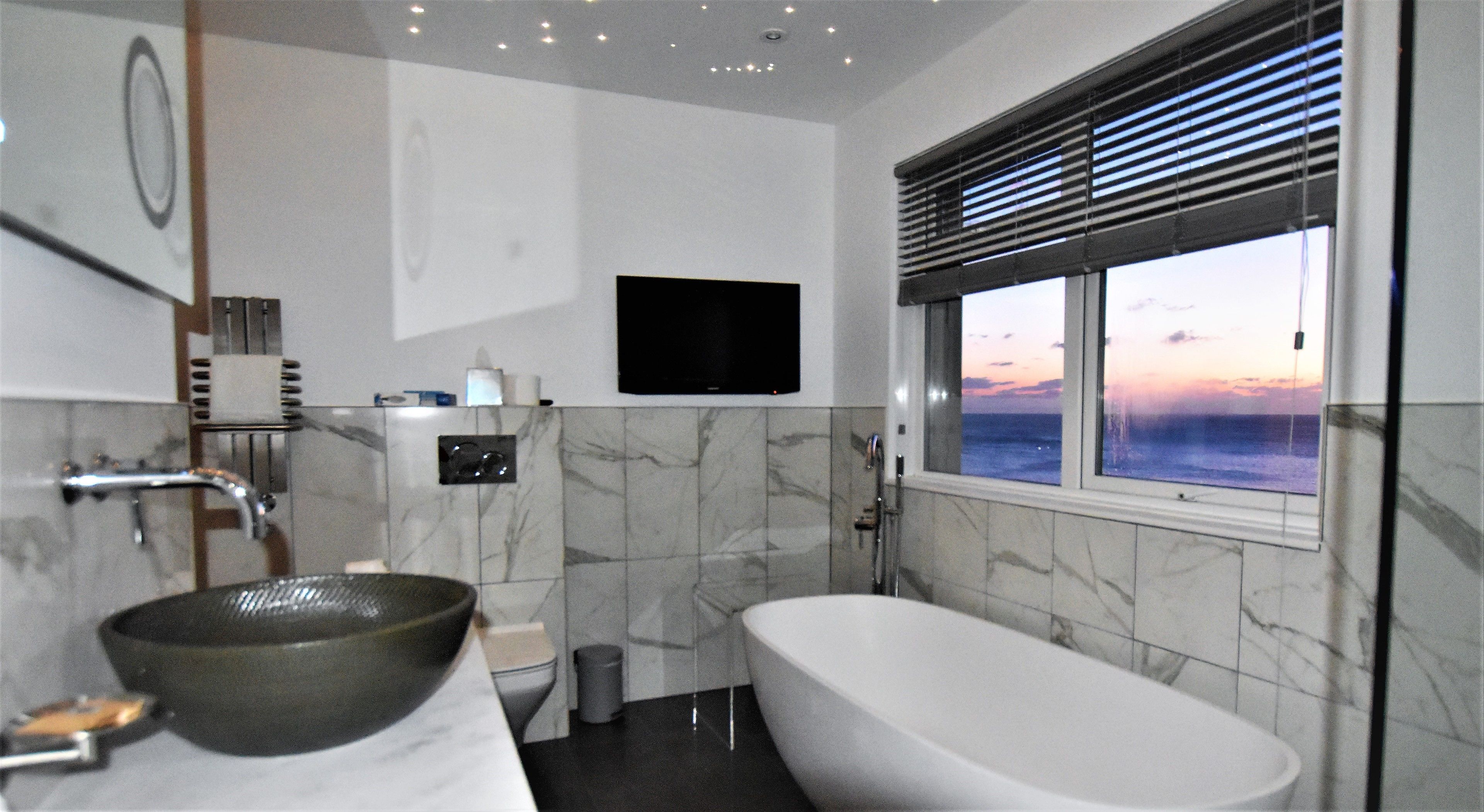 Een badkamer met een bad, een wastafel, een toilet, een douche en een televisie aan de muur.