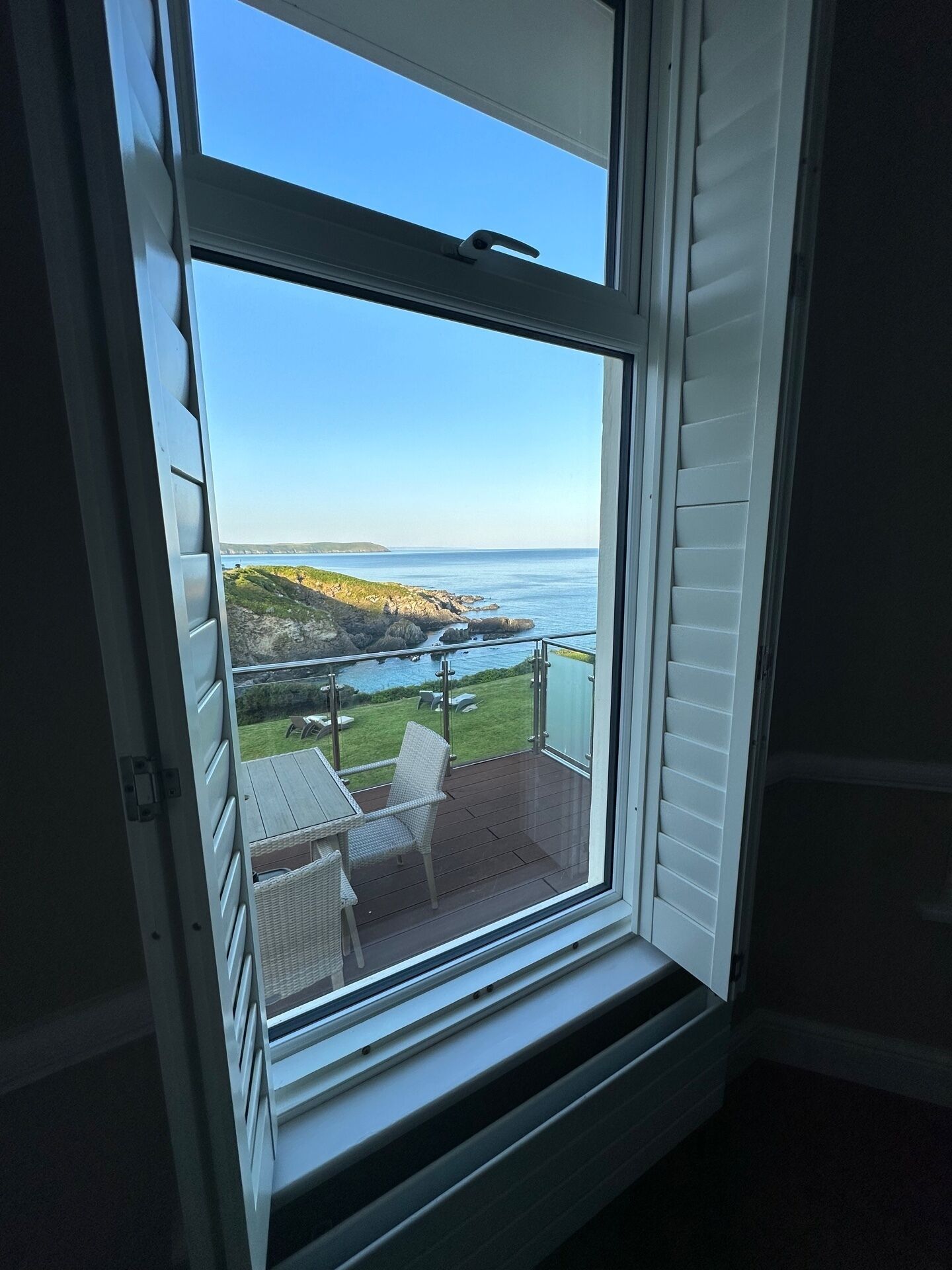 A room with a large window overlooking a coastal view, including a deck with outdoor furniture.