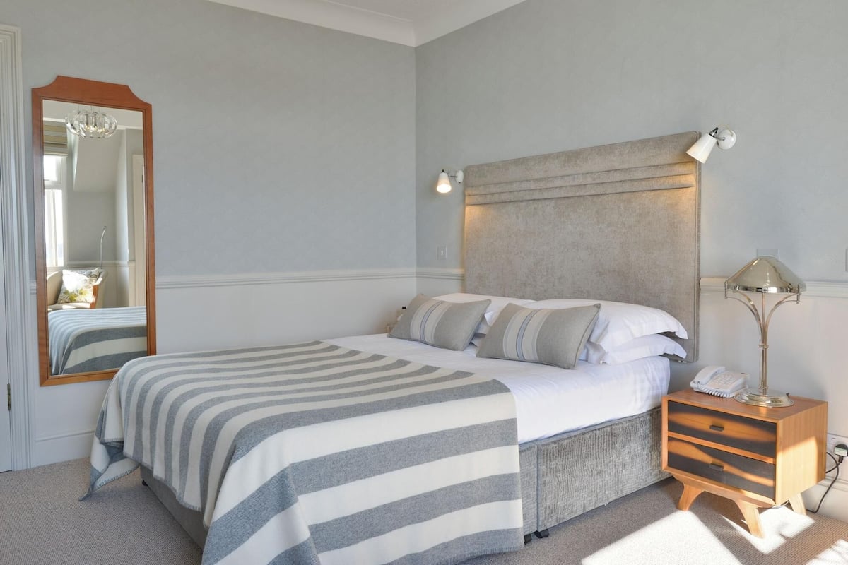Une chambre à coucher avec un lit, une table de chevet avec une lampe, un miroir et une tête de lit.