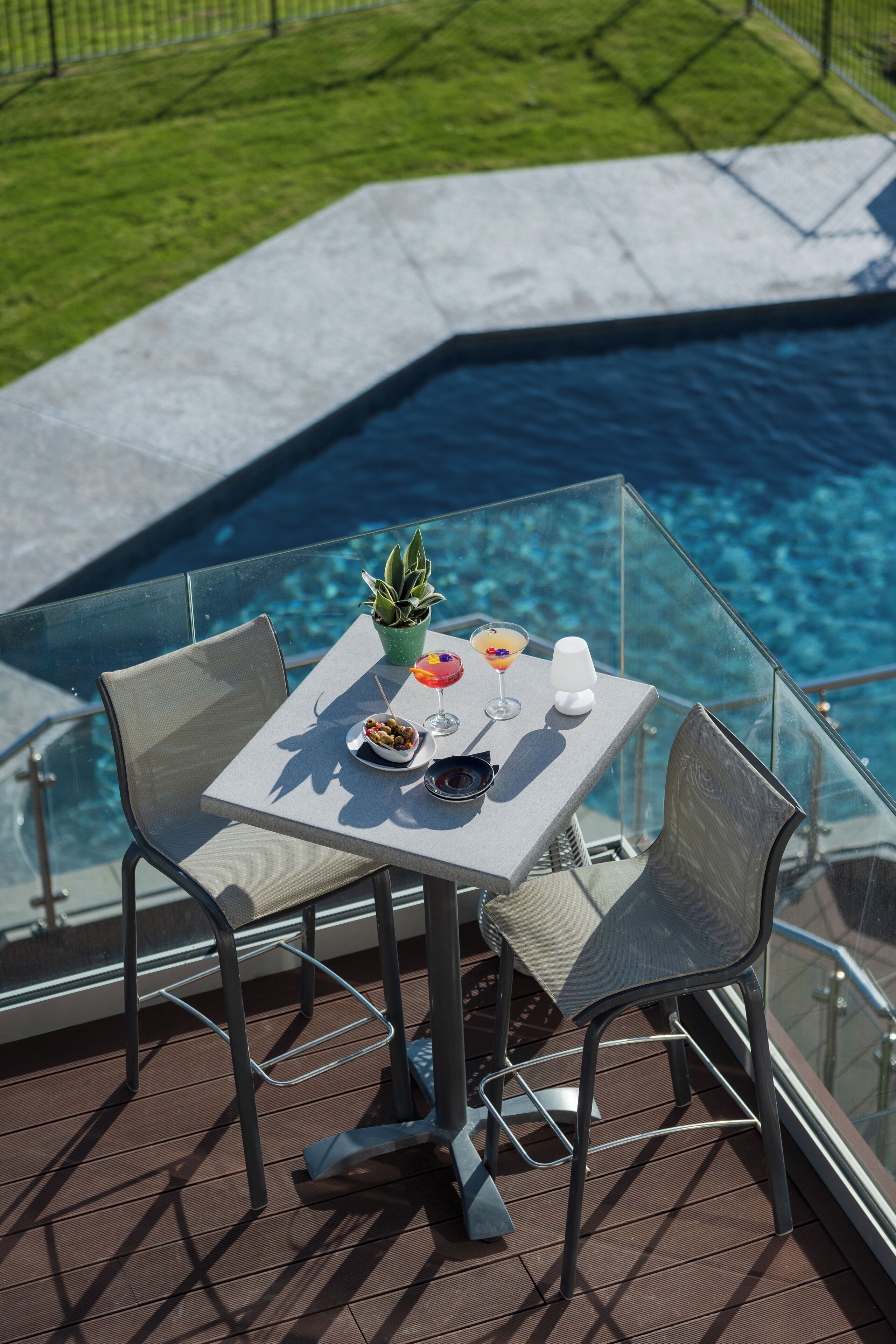 Ett glasbord med två stolar på en terrass med utsikt över en pool.