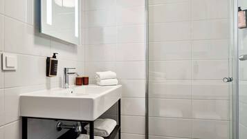Une salle de bain moderne avec un lavabo blanc, une douche en verre et des serviettes soigneusement pliées, rangées sur une étagère.