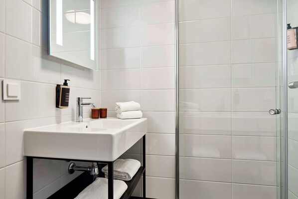 A modern bathroom with a white sink, a glass shower enclosure, and neatly folded towels on a shelf.