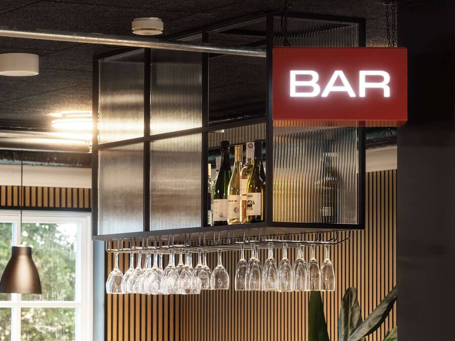 Zona de bar con un letrero que dice 'BAR', botellas de vino y copas en una estantería.