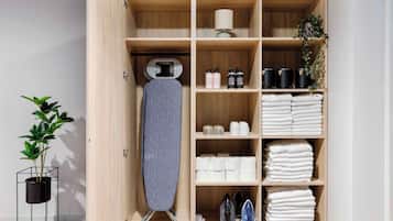 A wooden storage unit with shelves holding an ironing board, towels, toiletries, and a potted plant.