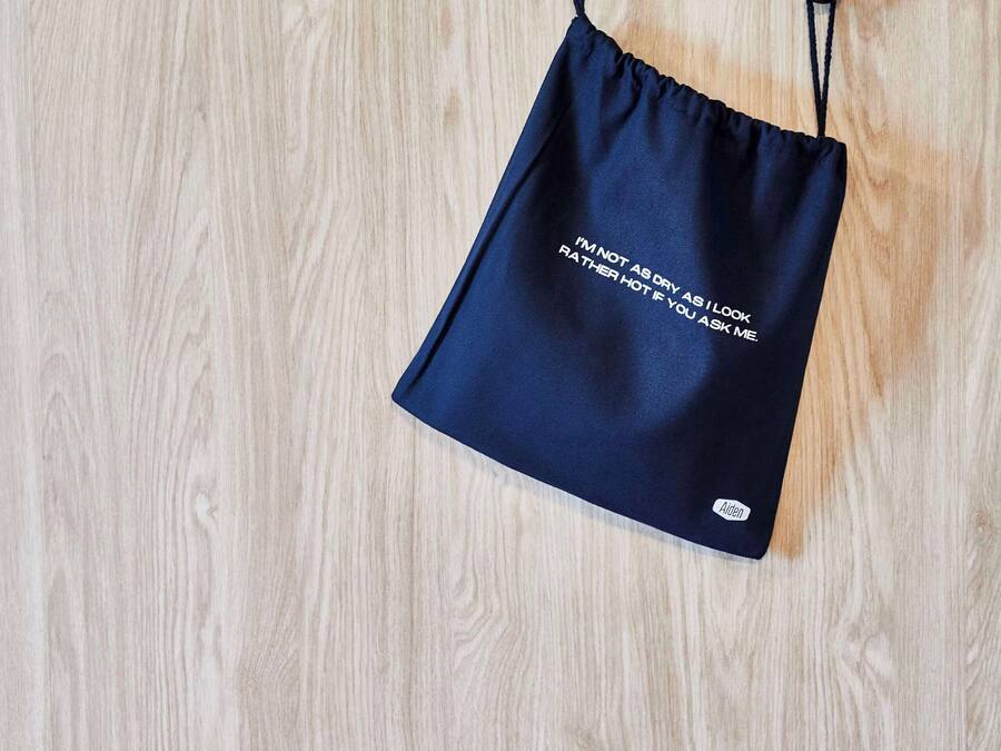 A navy blue drawstring bag with text on it, hanging on a wooden surface.