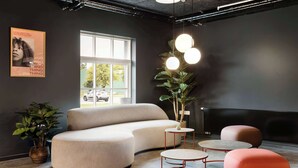 A modern lounge area with a curved sofa, round tables, and a large TV screen. - Aiden by Best Western Lolland (Holeby)