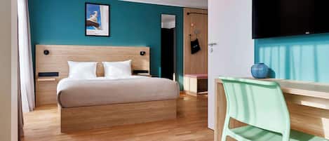 Habitación de hotel moderna con una cama de madera, un escritorio con silla, un televisor y una pared de acento color turquesa.