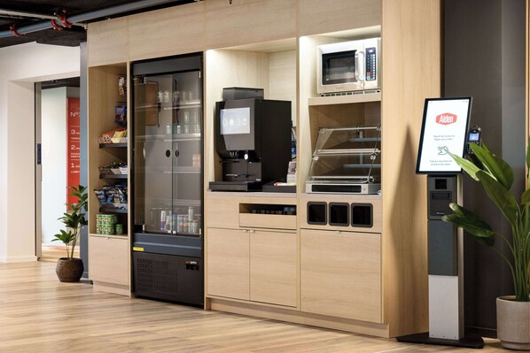 A modern kitchen area with a refrigerator, microwave, and a digital menu board.