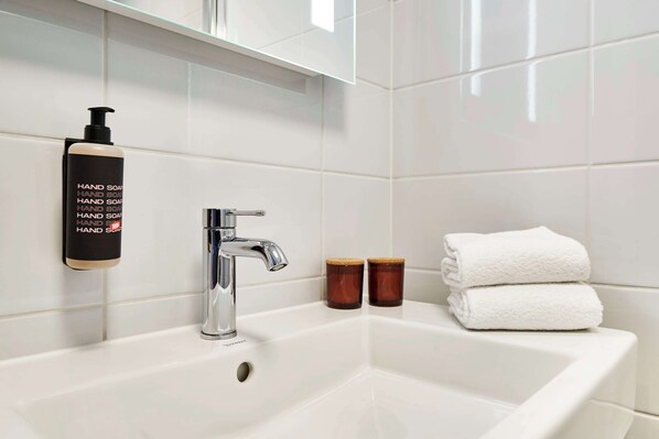 A bathroom with a white sink, a chrome faucet, a hand soap dispenser, two wooden cups, and two folded white towels.