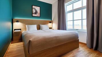 Una cama bien tendida en una habitación con paredes azul verdosas, un cabecero de madera y una ventana con cortinas.
