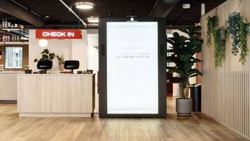 Ein Empfangsbereich mit einem 'CHECK IN'-Schild, einem digitalen Bildschirm und einem Empfischschalter mit einer Pflanze.
