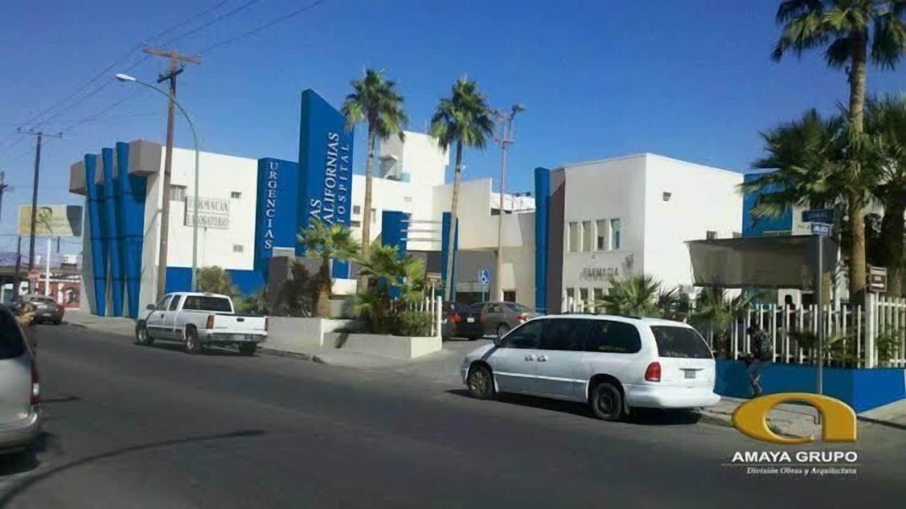 A building with a blue and white facade, palm trees, and parked cars.