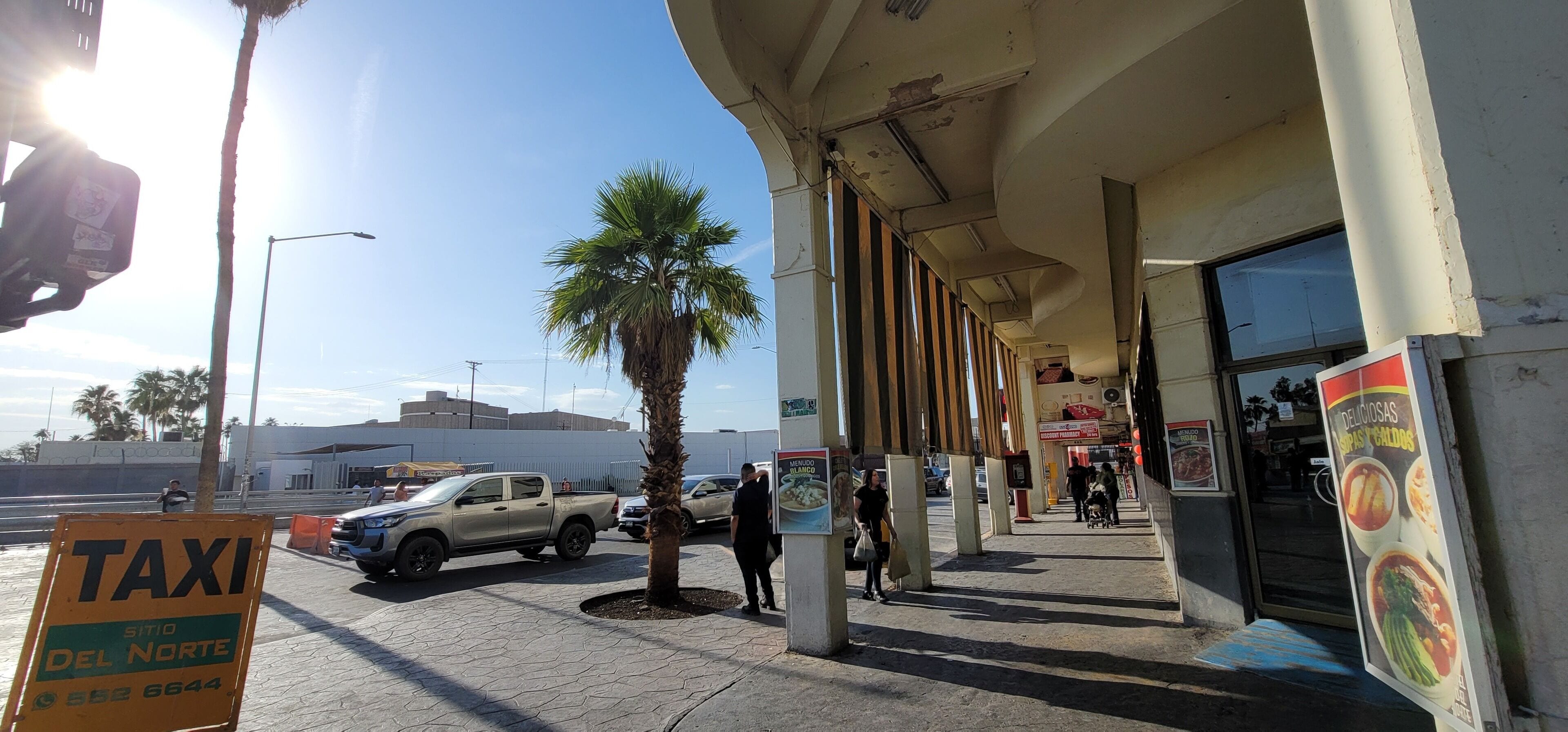 A street scene with a taxi sign, palm trees, and a building with a signboard.