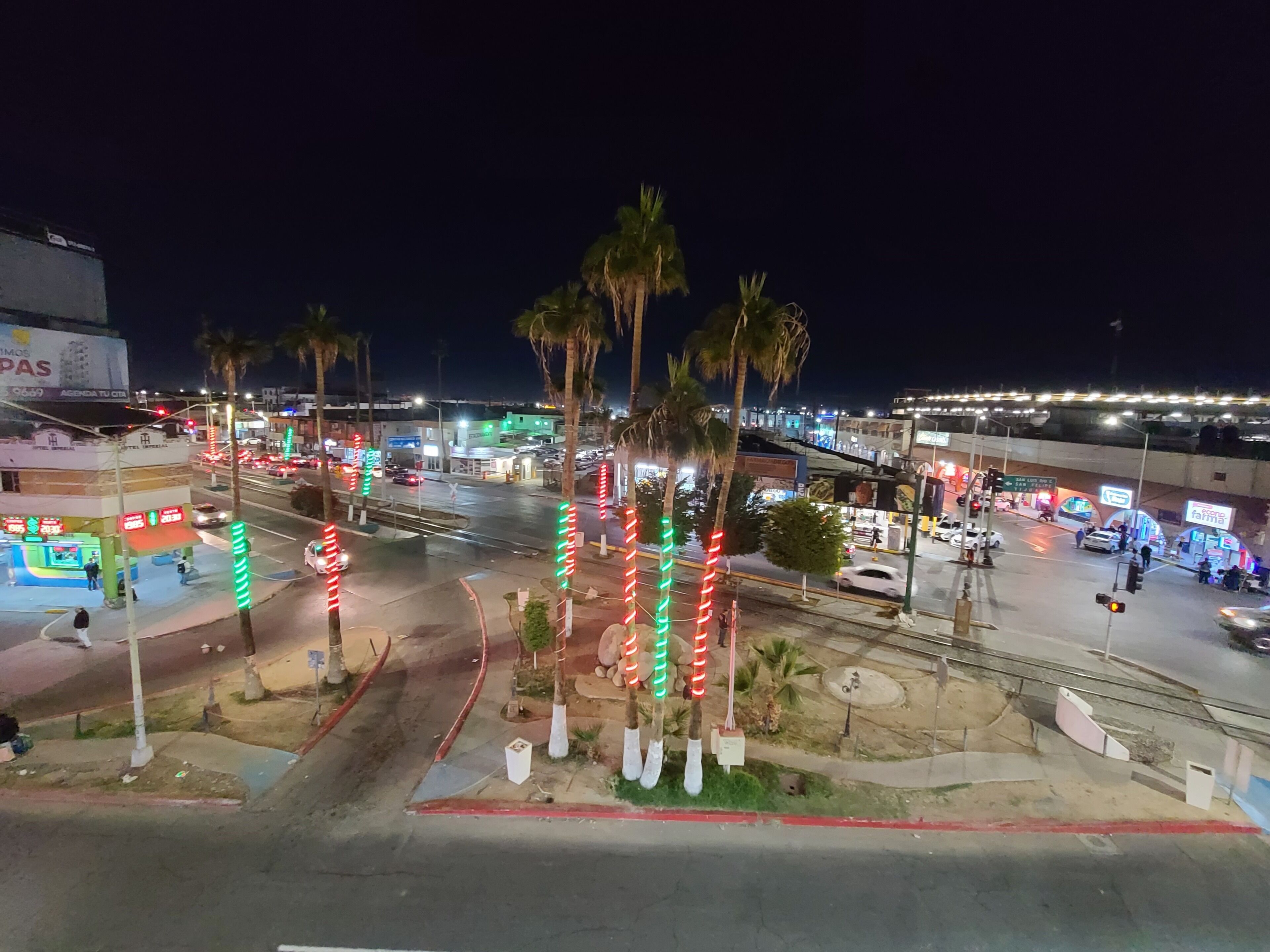 A nighttime cityscape with palm trees, street lights, and a busy intersection.