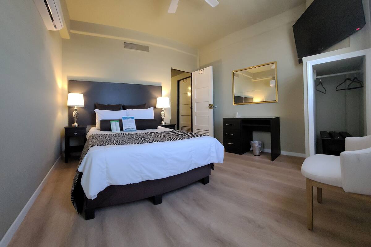 A hotel room with a bed, bedside tables, a ceiling fan, a TV, a wardrobe, and a mirror.