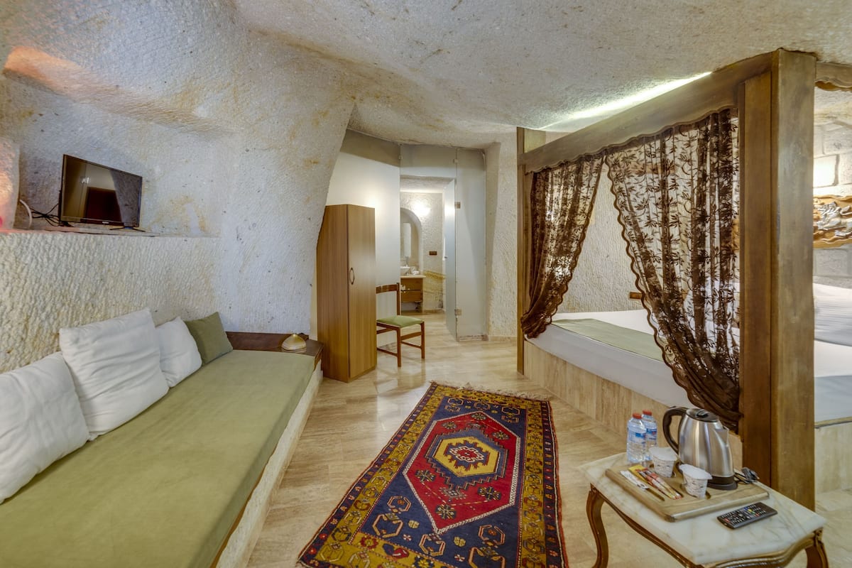 A cozy room with a bed, a small table with a kettle, and a TV on the wall.