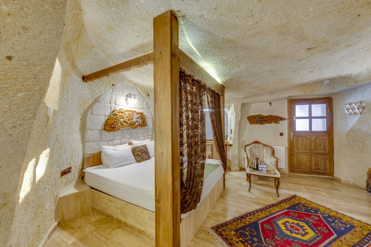 A bedroom with a four-poster bed, a wooden nightstand, a patterned rug, and a wooden door.